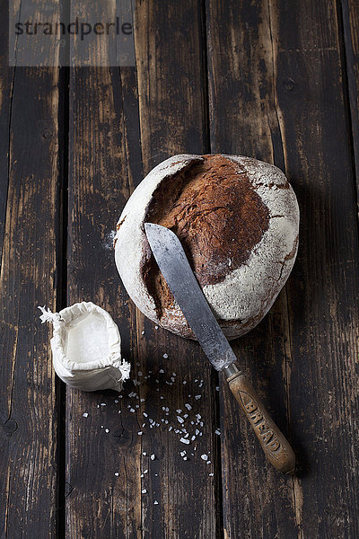 Knuspriges Brot  Brotmesser und Beutel mit Salzkörnern auf dunklem Holz