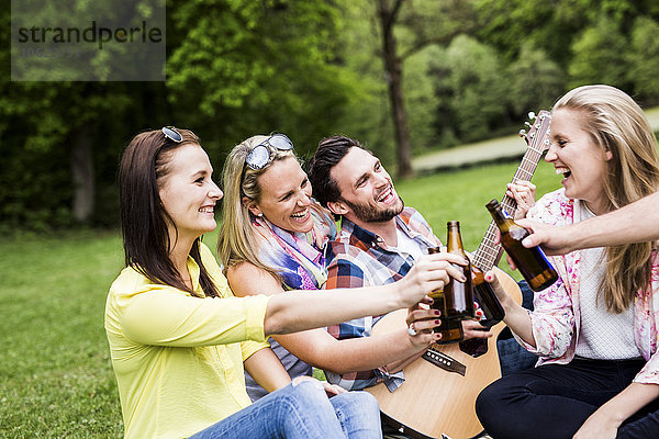 Glückliche Freunde klirren Bierflaschen im Park