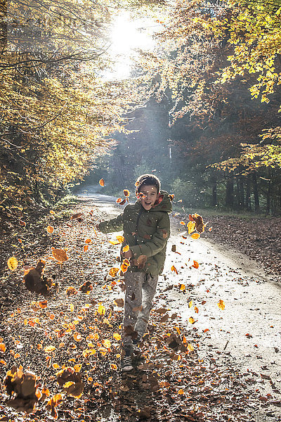 Junge spielt mit Blättern im Herbstwald