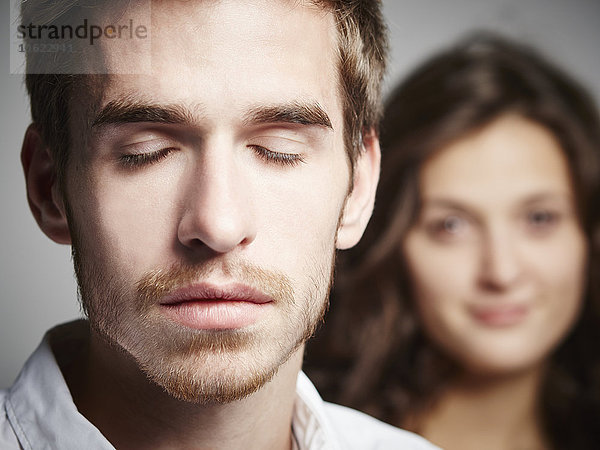 Porträt eines jungen Mannes mit geschlossenen Augen und Freundin im Hintergrund