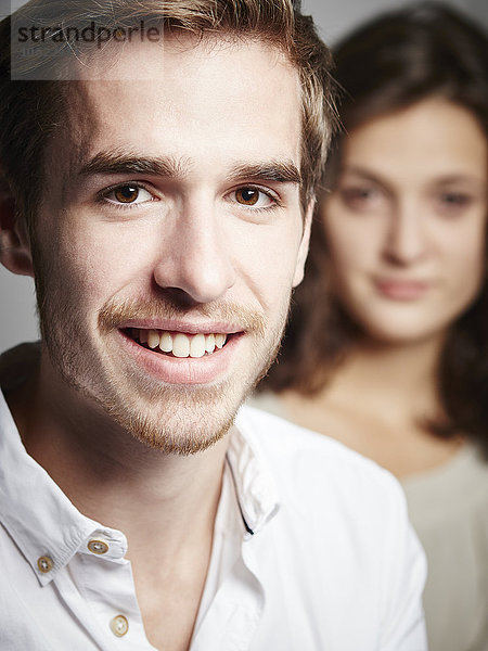 Portrait des lächelnden jungen Mannes mit Freundin im Hintergrund