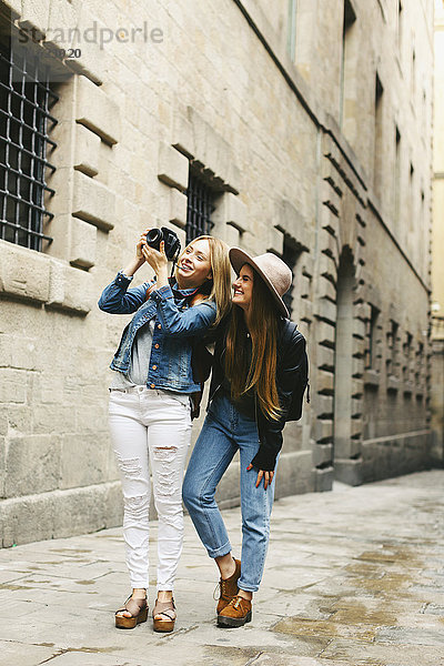 Spanien  Barcelona  zwei junge Frauen  die in der Stadt spazieren gehen und Fotos machen.