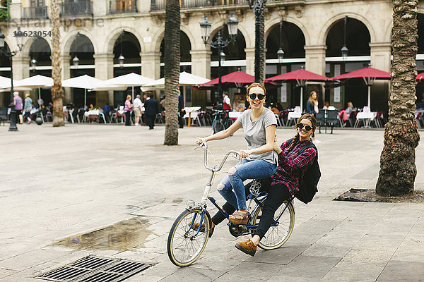 Spanien  Barcelona  zwei glückliche junge Frauen teilen sich das Fahrrad in der Stadt.