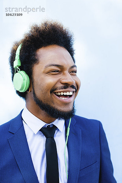 Porträt eines lächelnden jungen Geschäftsmannes  der Musik mit Kopfhörern hört.
