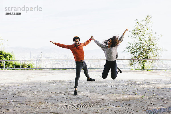Spanien  Barcelona  Portrait eines glücklichen jungen Paares  das auf der Aussichtsterrasse in die Luft springt.