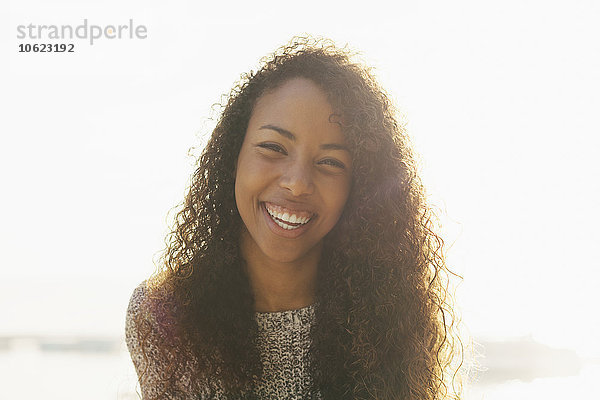 Porträt einer lächelnden jungen Frau mit lockigen braunen Haaren im Gegenlicht