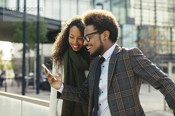 Zwei lächelnde junge Geschäftsleute im Freien  die auf das Smartphone schauen.
