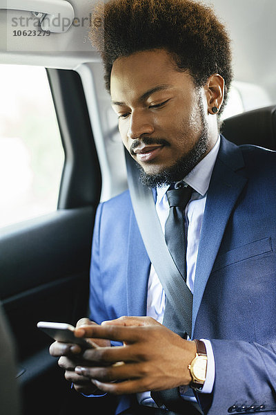 Geschäftsmann sitzt auf dem Rücksitz eines Autos und schaut auf das Smartphone.