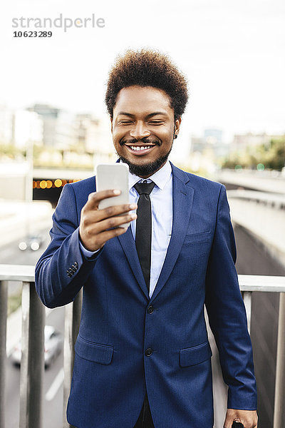 Porträt eines lächelnden Geschäftsmannes mit Blick auf sein Smartphone