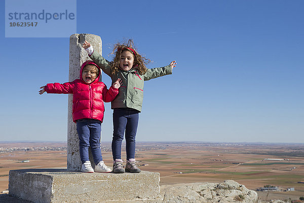 Spanien  Consuegra  zwei glückliche kleine Mädchen  die mit ausgestreckten Armen auf dem Gipfel stehen.