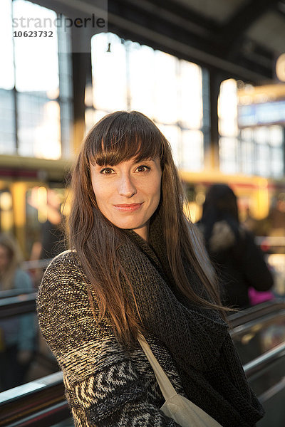Deutschland  Berlin  Porträt einer lächelnden jungen Frau  die am Bahnsteig wartet