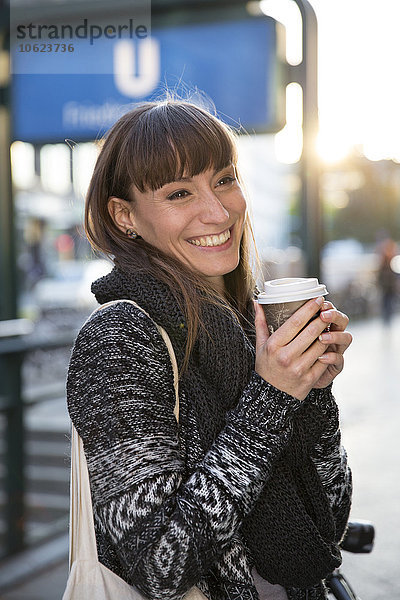 Deutschland  Berlin  lächelnde junge Frau mit Kaffee zum Mitnehmen