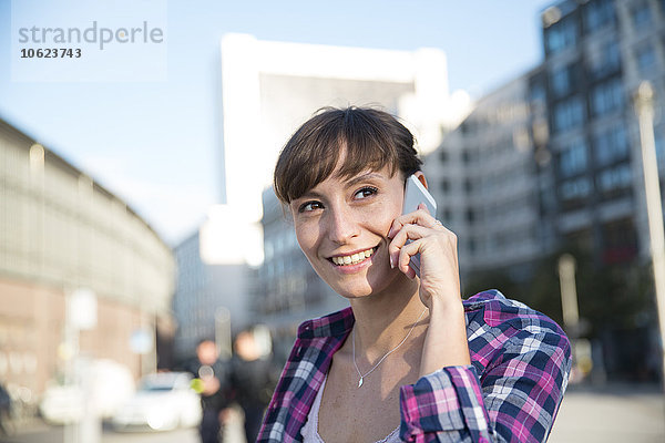 Deutschland  Berlin  Portrait einer jungen Frau beim Telefonieren mit dem Smartphone
