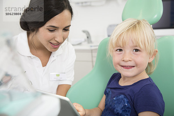 Zahnarzt und lächelndes Mädchen mit digitalem Tablett im Zahnarztstuhl