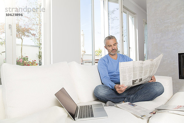 Erwachsener Mann zu Hause  auf der Couch sitzend  Zeitung lesend
