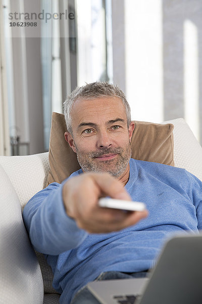 Erwachsener Mann auf der Couch mit Laptop  mit Fernbedienung