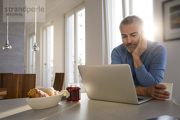 Erwachsener Mann  der von zu Hause aus mit dem Laptop arbeitet