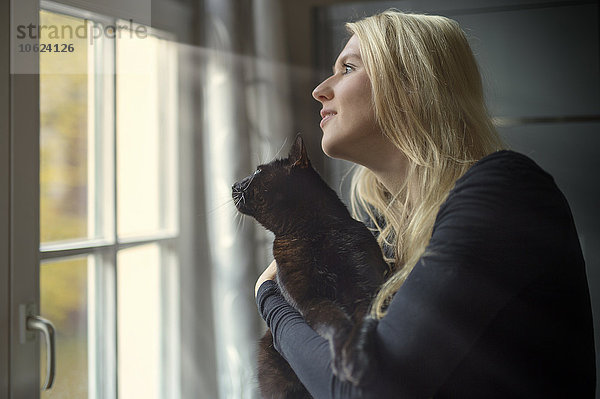 Frau und Katze schauen zu Hause durchs Fenster