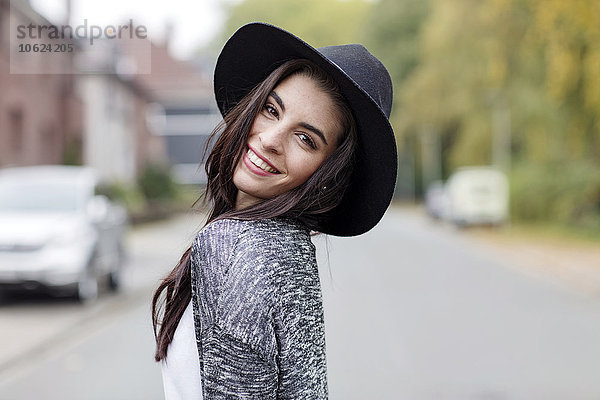 Porträt einer lächelnden jungen Frau mit schwarzem Hut über die Schulter schauend