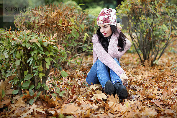 Junge Frau in Herbstmode auf dem mit Herbstblättern bedeckten Boden sitzend