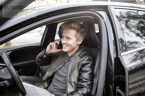 Lächelnder junger Mann im Auto am Handy