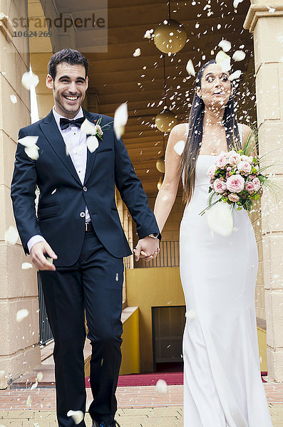 Brautpaar nach der Hochzeit bei Regen von Rosenblättern und Reiskörnern