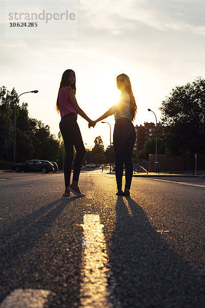 Zwei Freundinnen  die Hand in Hand bei Gegenlicht stehen.