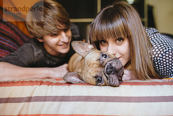 Junges Paar  das mit seiner französischen Bulldogge auf dem Bett liegt.