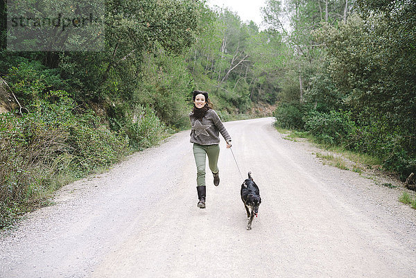 Lächelnde Frau rennt mit ihrem Hund auf einer Bergstraße