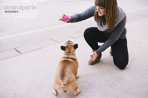 Junge Frau spielt mit ihrer französischen Bulldogge auf dem Bürgersteig