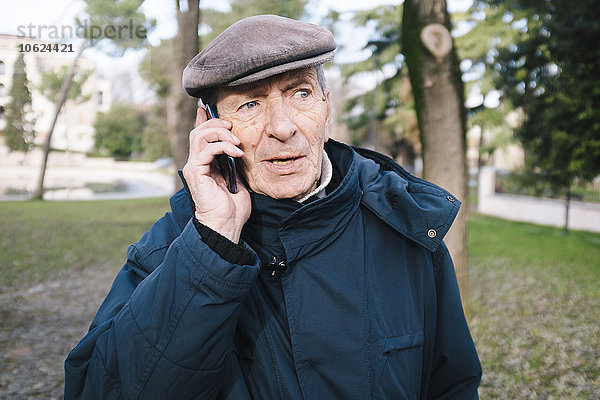 Porträt eines älteren Mannes  der mit einem Smartphone im Park telefoniert.