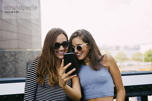 USA  New York City  zwei lächelnde Freunde beim Blick aufs Handy