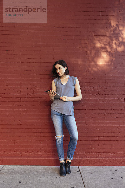 Porträt einer Frau mit digitalem Tablett an der roten Ziegelwand lehnend