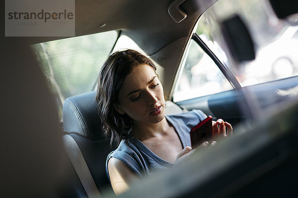 Porträt einer jungen Frau  die mit ihrem Smartphone in einem Taxi sitzt.