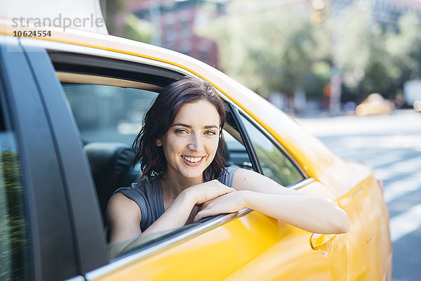 USA  New York City  Porträt einer lächelnden jungen Frau in einem gelben Taxi