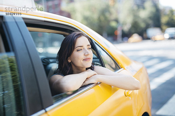 USA  New York City  Porträt einer jungen Frau  die sich aus dem Fenster eines gelben Taxis lehnt.