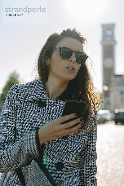 Italien  Vicenza  Frau mit kariertem Mantel und Sonnenbrille mit Mobiltelefon