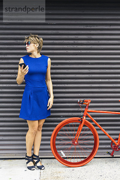 Frau mit Smartphone und rotem Rennrad wartet auf den Rollladen