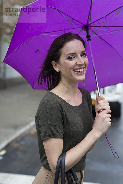USA  New York City  Porträt einer lächelnden jungen Frau mit Regenschirm an einem Regentag