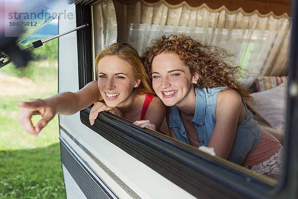 Zwei Freundinnen  die durch das Fenster des Wohnwagens schauen und etwas sehen.