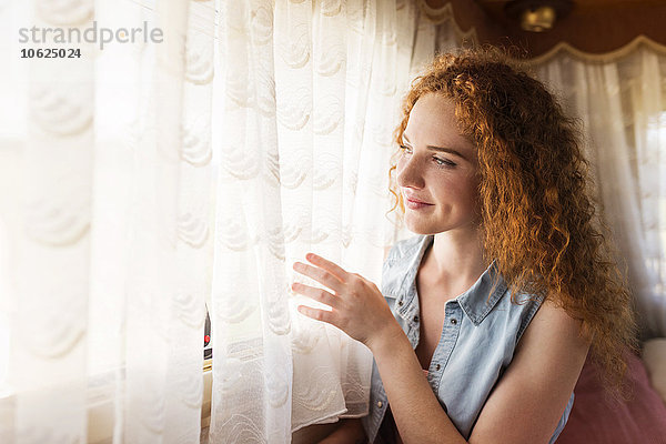 Lächelnde junge Frau sitzt in einem Wohnwagen und schaut durchs Fenster.