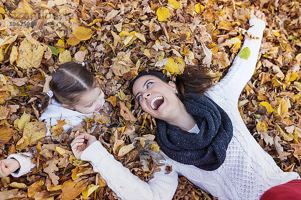 Glückliches Mädchen mit Mutter im Herbstlaub liegend