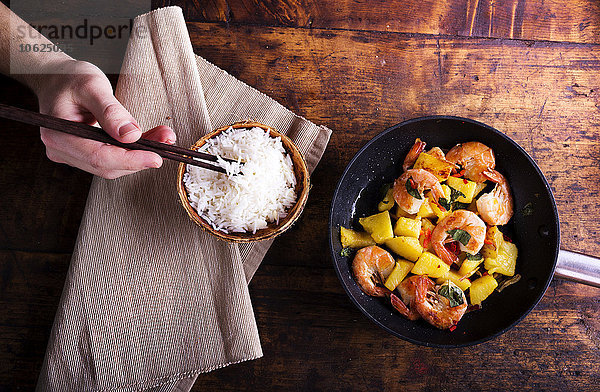 Garnelenpfanne mit Ananas und Männerhand mit Reis und Essstäbchen