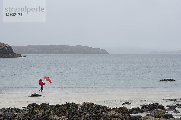 UK  Schottland  Isle of Skye  wandelndes Mädchen mit Regenschirm am regnerischen und stürmischen Strand