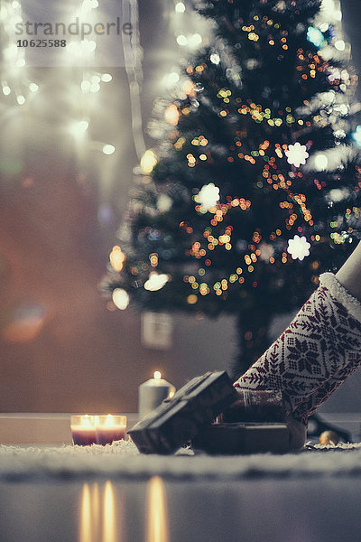 Weihnachtsgeschenke auf dem Teppich liegend vor dem beleuchteten Weihnachtsbaum