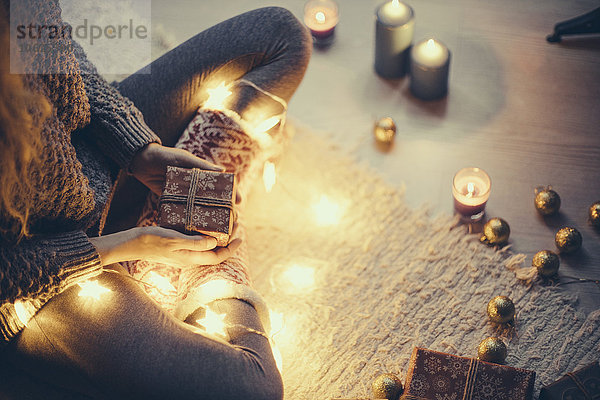Frau sitzend mit Weihnachtsgeschenk und Lichterkette auf dem Teppich