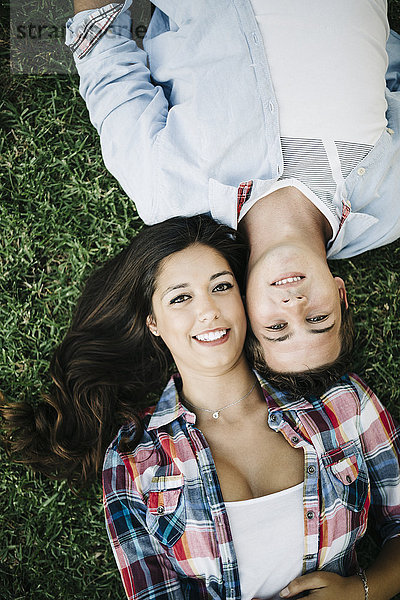 Porträt eines verliebten jungen Paares  das Kopf an Kopf auf einer Wiese liegt.