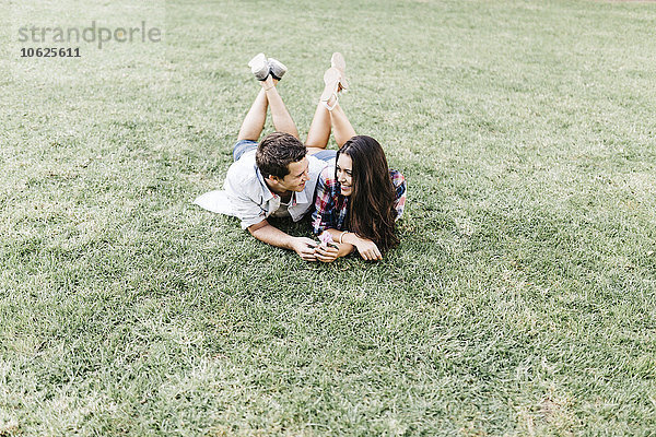 Verliebtes junges Paar liegt auf einer Wiese in einem Park und schaut sich an.