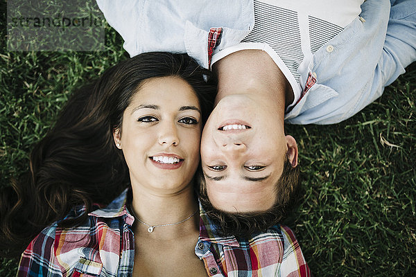Porträt eines verliebten jungen Paares  das Kopf an Kopf auf einer Wiese liegt.