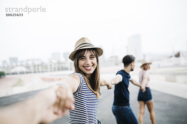 Spanien  Barcelona  Porträt einer lächelnden jungen Frau  die mit ihren Freunden Händchen hält.
